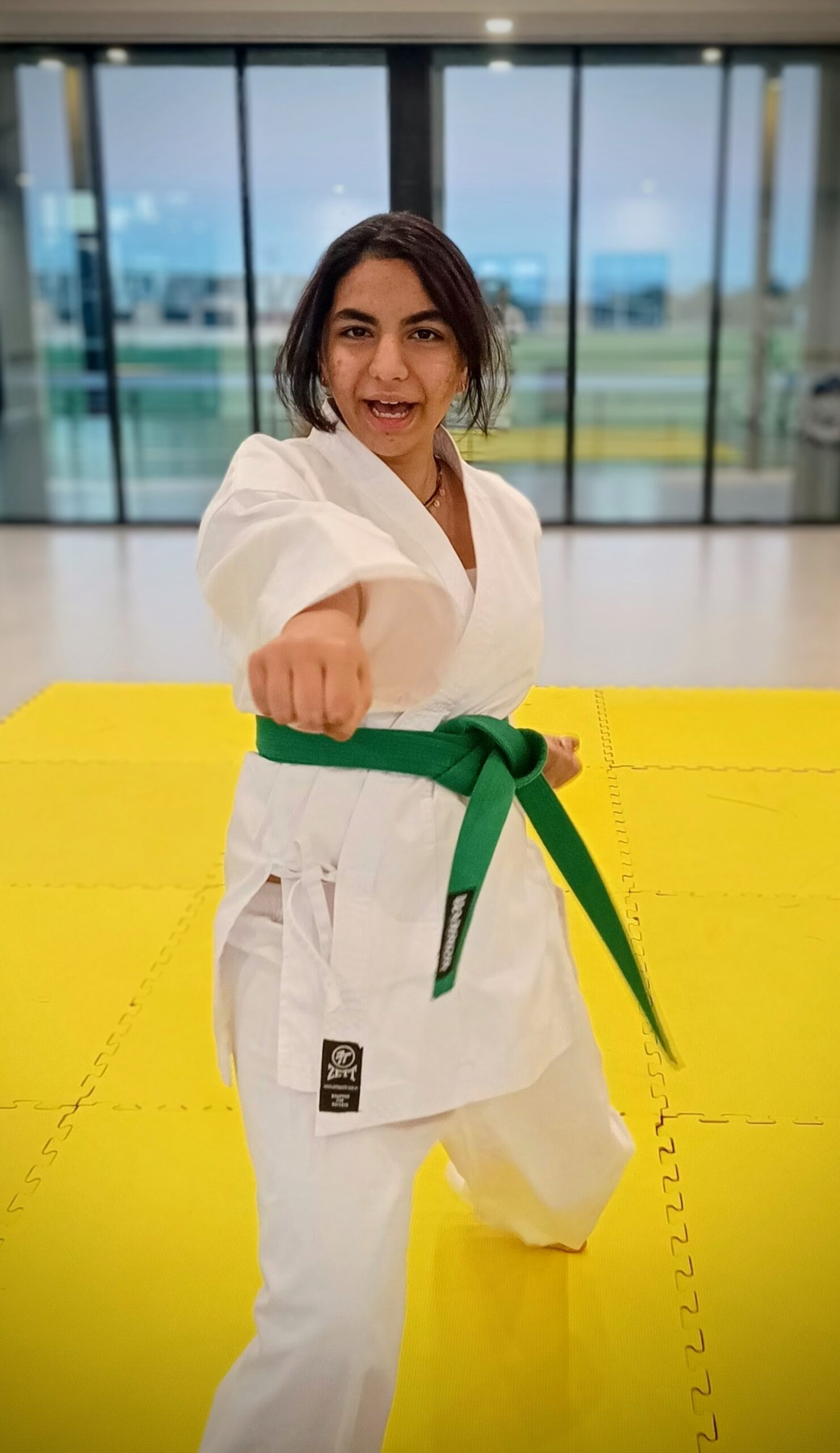 A teenage girl in green belt punches towards the camera