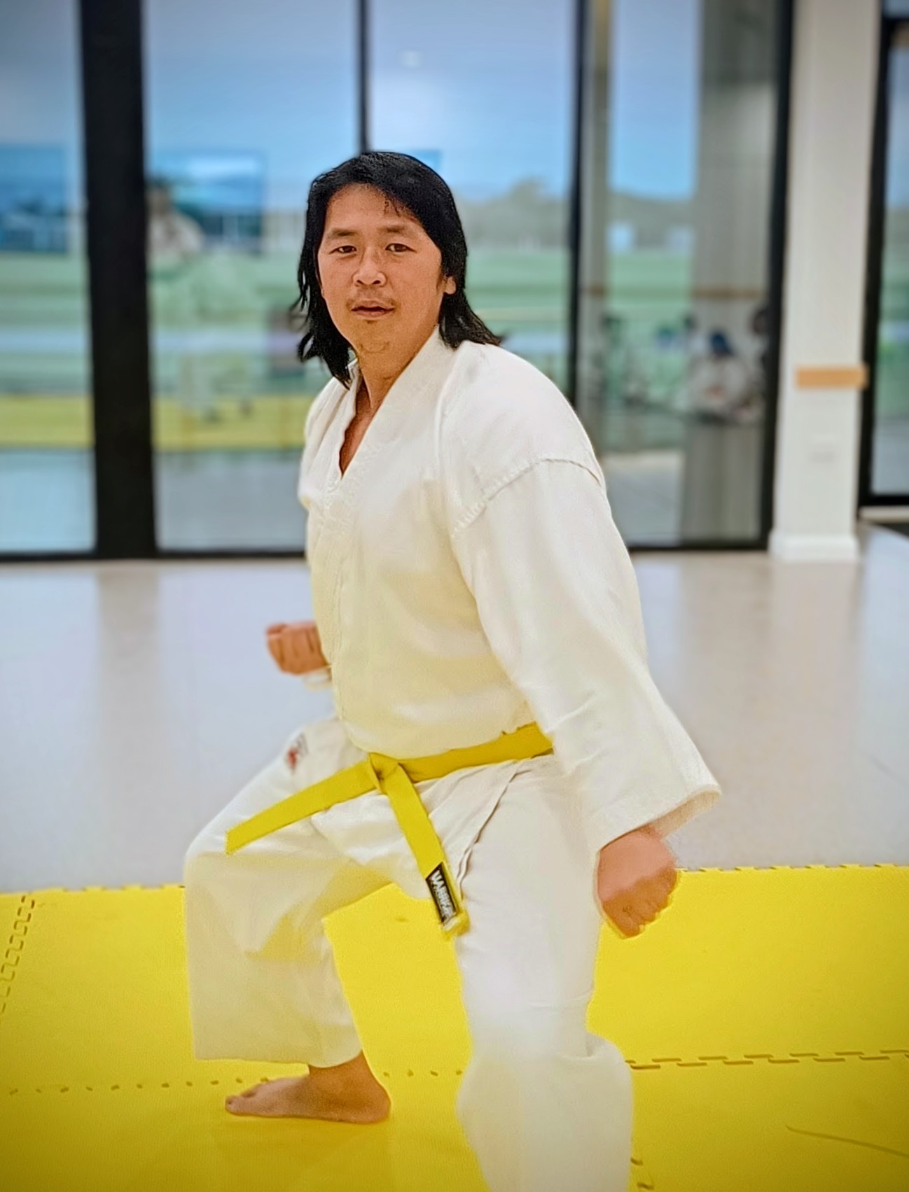 A man in karate uniform and yellow belt performs a low block