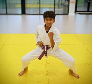A young boy in karate uniform in sumo stance performing a downward elbow strike