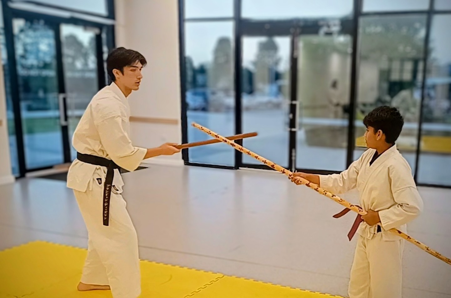 A karate instructor and a young student cross bo staff on a yellow matt