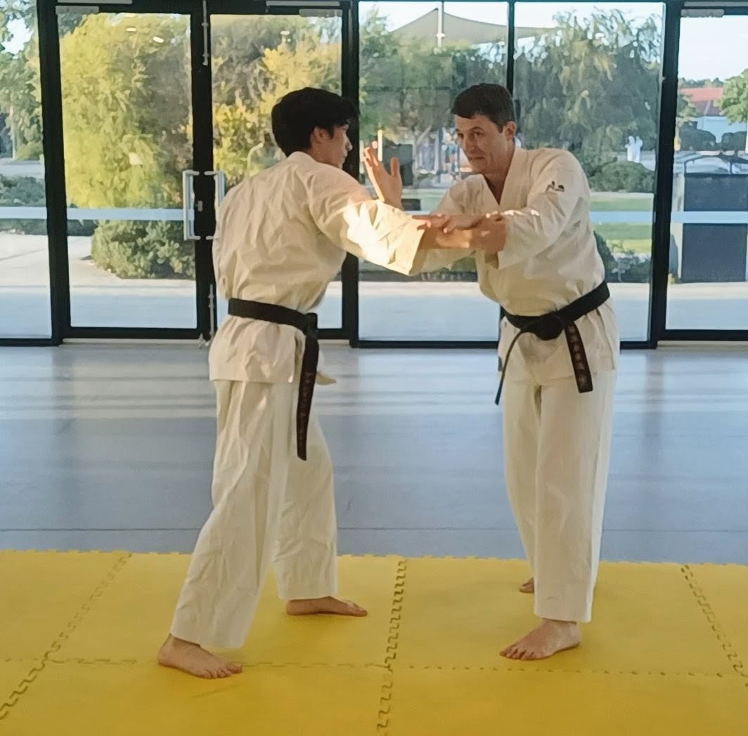 Two men demonstrating a karate technique on yellow matts